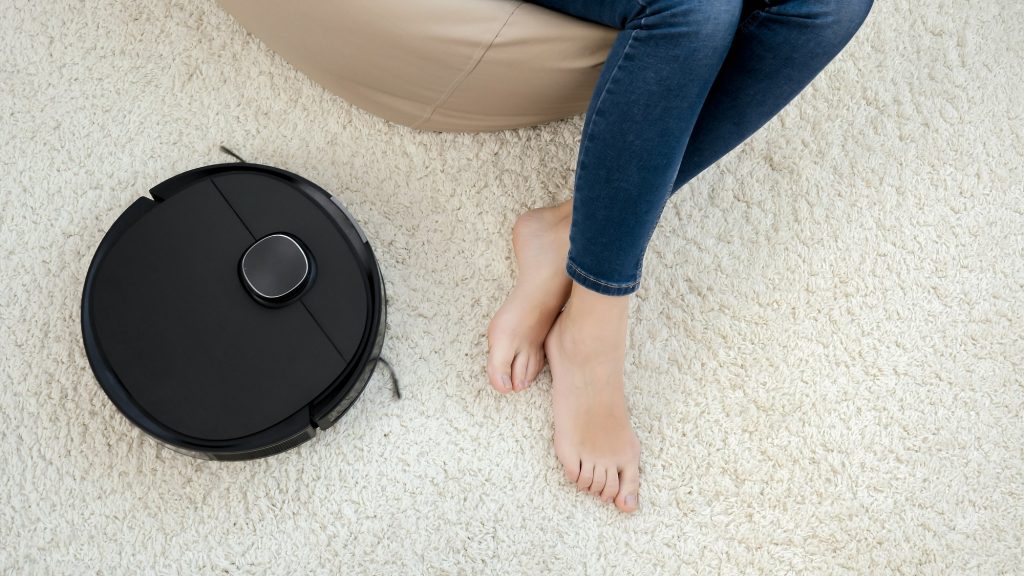 Closeup of robot vacuum cleaner doing housework and cleanup around woman relaxing in chair at living