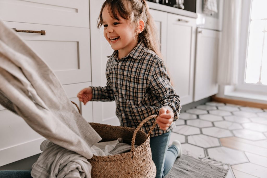 Little girl laughs and holds handles of knitted laundry basket